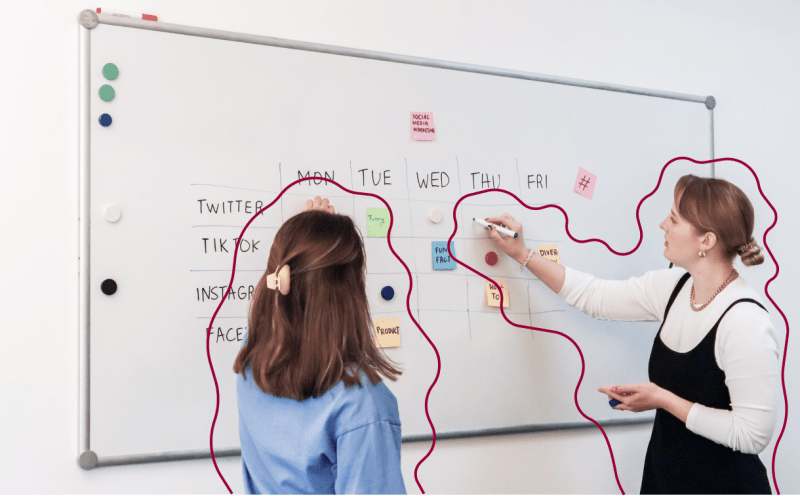 Photo of two women standing at a white board plotting out a content calendar for various social media channels